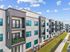 Modern apartment complex with stylish balconies, sleek black and white exterior, and beautifully landscaped green spaces under a bright blue sky.