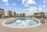 Modern apartment complex with a luxurious outdoor pool area, surrounded by stylish lounge chairs and umbrellas against a clear blue sky.