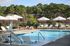 Inviting outdoor pool area with elegant lounge chairs and umbrellas, surrounded by lush greenery, perfect for relaxation.