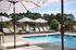 Charming outdoor pool area with elegant lounge chairs and stylish umbrellas set against a lush green backdrop.