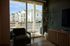 Inviting apartment interior with large glass doors opening to a serene view of modern townhouses, complemented by charming decor and natural light.