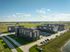 Aerial view of modern apartment complex surrounded by lush greenery and open fields, offering a serene residential environment.