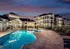 Luxurious apartment complex with stylish architecture and a sparkling pool under a vibrant sunset sky.