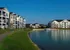 Charming apartment buildings with modern architecture overlook a serene pond under a clear blue sky, offering a picturesque and tranquil living environment.