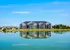 Stunning lakeside apartment complex under a clear blue sky with beautiful reflections on the water, offering serene and picturesque views.
