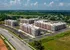 Aerial view of modern luxury apartment complex with multiple buildings, ample parking, and lush green surroundings under a bright blue sky.