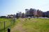 Modern apartment complex with vibrant red and beige buildings, set next to a scenic grassy park area, ideal for outdoor activities.