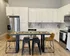Modern kitchen with sleek white cabinetry, stainless steel appliances, and a chic dining area with stylish seating on wood flooring.