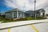 Charming exterior view of a modern single-story community building with large windows, surrounded by lush landscaping under a vibrant blue sky.