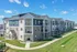 Elegant three-story apartment building with modern design, large balconies, and surrounding lush green lawns under a bright blue sky.