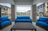 Inviting outdoor seating area overlooking a sparkling pool with vibrant blue cushions against a backdrop of modern apartment buildings.