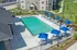 Luxurious apartment complex with a pristine swimming pool, vibrant blue umbrellas, and stylish lounge chairs, set against lush green landscaping.