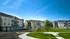 Charming modern apartment complex surrounded by lush greenery and bright blue sky, offering spacious living with balcony views and ample parking.
