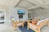 Chic outdoor living area featuring modern wooden furniture, a cozy stone fireplace, and a large TV, perfect for relaxing and entertaining.