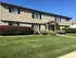 Beautiful two-story apartment building with manicured shrubs and lush green lawn under a bright blue sky.