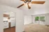 Bright apartment interior with elegant ceiling fan, cozy kitchen, and inviting living space opening to a balcony with lush greenery.