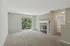 Spacious living room with a cozy fireplace, large windows offering lush green views, and plush carpeting, perfect for relaxation and entertaining.