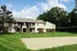 Charming suburban apartment building surrounded by lush greenery, featuring spacious balconies and a sandy volleyball court in a serene outdoor setting.