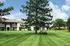 Charming apartment complex with lush green lawns, mature trees, and inviting outdoor seating for relaxation under a bright blue sky.