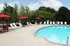 Inviting outdoor pool area with bright blue water, surrounded by lush greenery and vibrant red umbrellas, offering a perfect spot for relaxation.