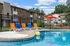 Inviting apartment complex with a sparkling pool, vibrant lounge chairs, and a charming patio with a red umbrella, perfect for relaxation.