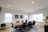 Elegant meeting room with a large wooden table, stylish chairs, and natural light from two windows, complemented by tasteful decor and vibrant greenery.