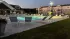 Elegant residential complex with covered swimming pool, modern clubhouse, and lush landscaping under a bright blue sky.