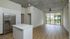 Modern open-concept apartment showcasing sleek kitchen with stainless steel refrigerator and spacious living area with large windows and scenic outdoor view.