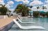 Luxurious pool area with elegant sun loungers, surrounded by lush palm trees and stylish cabanas under a bright blue sky.