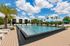 Luxurious outdoor pool area with palm trees, sun loungers, and shaded umbrellas, under a clear blue sky.