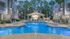 Elegant evening view of a luxurious apartment complex with a sparkling swimming pool, stylish loungers, and lush palm trees, offering serene and upscale outdoor living.
