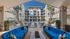 Luxurious apartment complex with a resort-style swimming pool, elegant outdoor seating area, and lush palm trees under a clear blue sky.