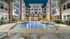 Luxurious apartment complex featuring a beautifully lit pool surrounded by elegant lounge chairs, with modern architecture and palm trees under the night sky.