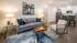 Modern open-concept living room with elegant decor, featuring a chic sofa, unique wood coffee table, and sleek kitchen bar area with stylish seating.