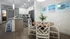 Chic open-plan kitchen and dining area with modern white cabinetry, sleek countertops, and stylish wicker chairs. Bright and airy with vibrant beach artwork adorning the walls, perfect for coastal living enthusiasts.