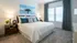 Elegant bedroom with cozy king-sized bed, stylish blue and white decor, and abundant natural light from large windows.