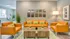 Inviting living room with vibrant orange sofas, green accent pillows, and stylish wood coffee tables, complemented by modern artwork and lush indoor plants.