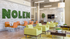 Modern communal lounge with stylish green armchairs, vibrant orange dining chairs, and a living wall sign creating an inviting atmosphere.