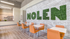 Modern communal space with vibrant orange seating, elegant white tables, and a striking greenery wall feature.