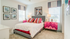 Bright, modern bedroom with vibrant decor, featuring a cozy bed, colorful pillows, stylish artwork, and natural light streaming through two windows.