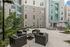 Chic apartment courtyard with modern seating, lush greenery, BBQ grills, and a cozy fire pit under stylish umbrellas.