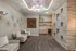 Elegant sitting area featuring plush beige chairs, modern decor, and textured wood accent wall, illuminated by a luxurious chandelier.