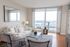 Elegant living room with panoramic city views, featuring chic white decor, modern furniture, and a sunlit ambiance.