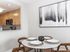 Chic dining area with modern round table, elegant place settings, and a view into a sleek kitchen featuring light wood cabinetry and stainless steel appliances.