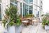 Chic outdoor patio with a wooden dining set, lush greenery, and vibrant flowers, perfect for relaxation and entertaining.