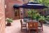Charming courtyard with wooden seating and navy umbrella, surrounded by lush greenery at The St. James entrance.