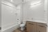 Sleek and modern bathroom with elegant fixtures, featuring a spacious tub-shower combo, pristine white tile, and contemporary wood cabinetry.