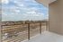 Spacious apartment balcony with modern railing offers stunning panoramic views of a scenic landscape under a bright blue sky.