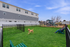 Vibrant apartment complex with lush green dog park, featuring a playful dog and a relaxing seating area near a children's playground.