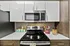 Modern kitchen featuring sleek white cabinetry, stainless steel appliances, and stylish decor with pops of color from a pink vase and candy jar.